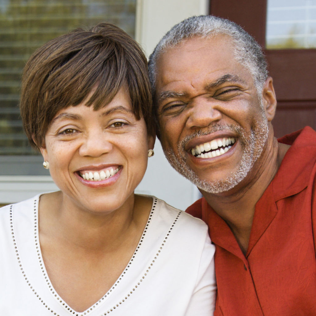 Couple sitting on outdoor steps of home smiling. Vertically framed shot.